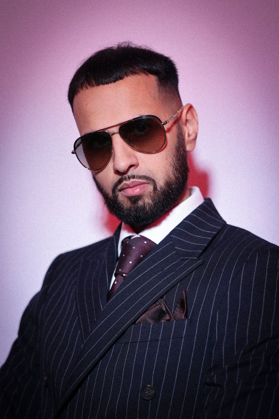 DJ Rish in a pinstripe suit against a pink backdrop