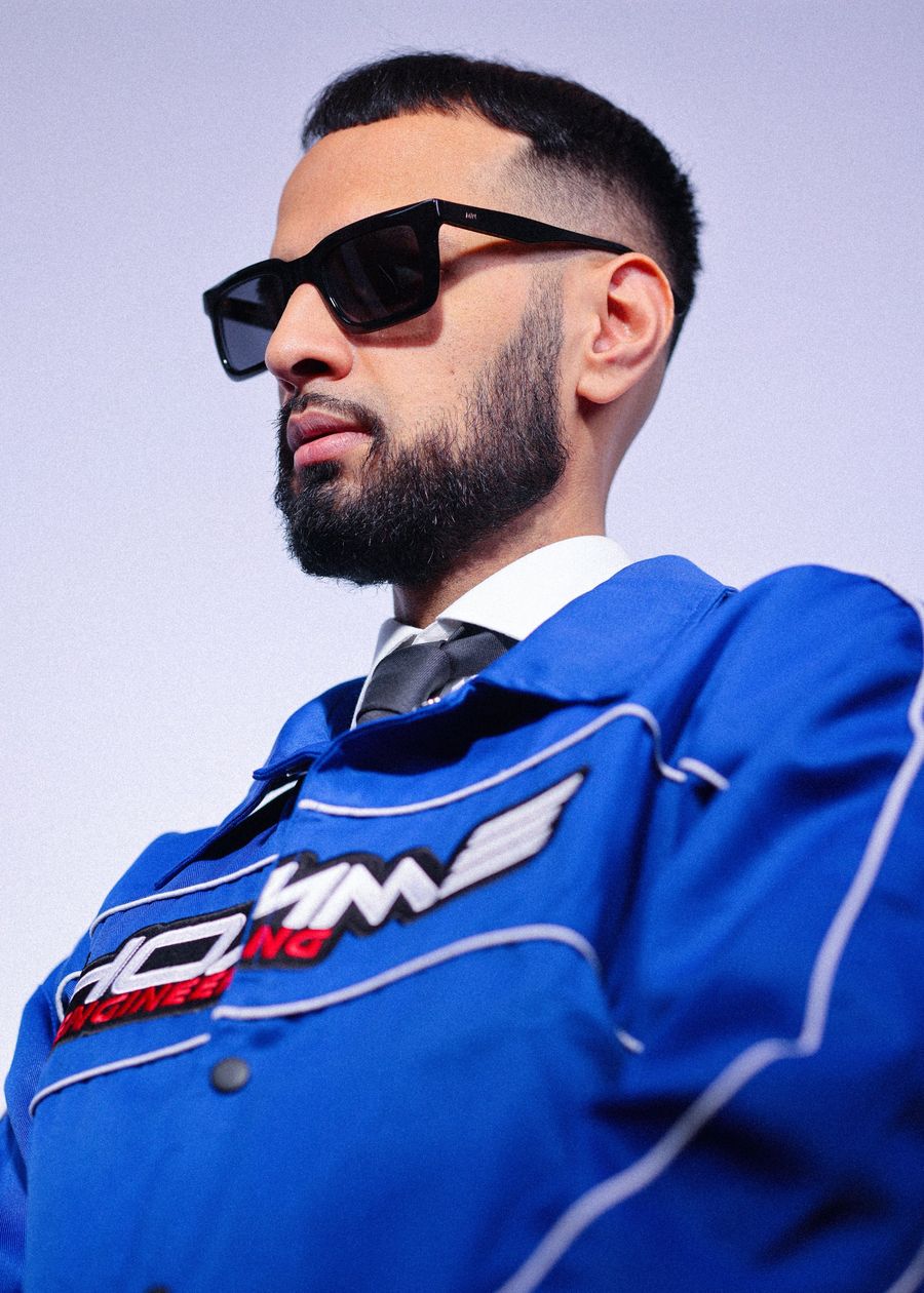DJ Rish in a blue racing jacket and black sunglasses